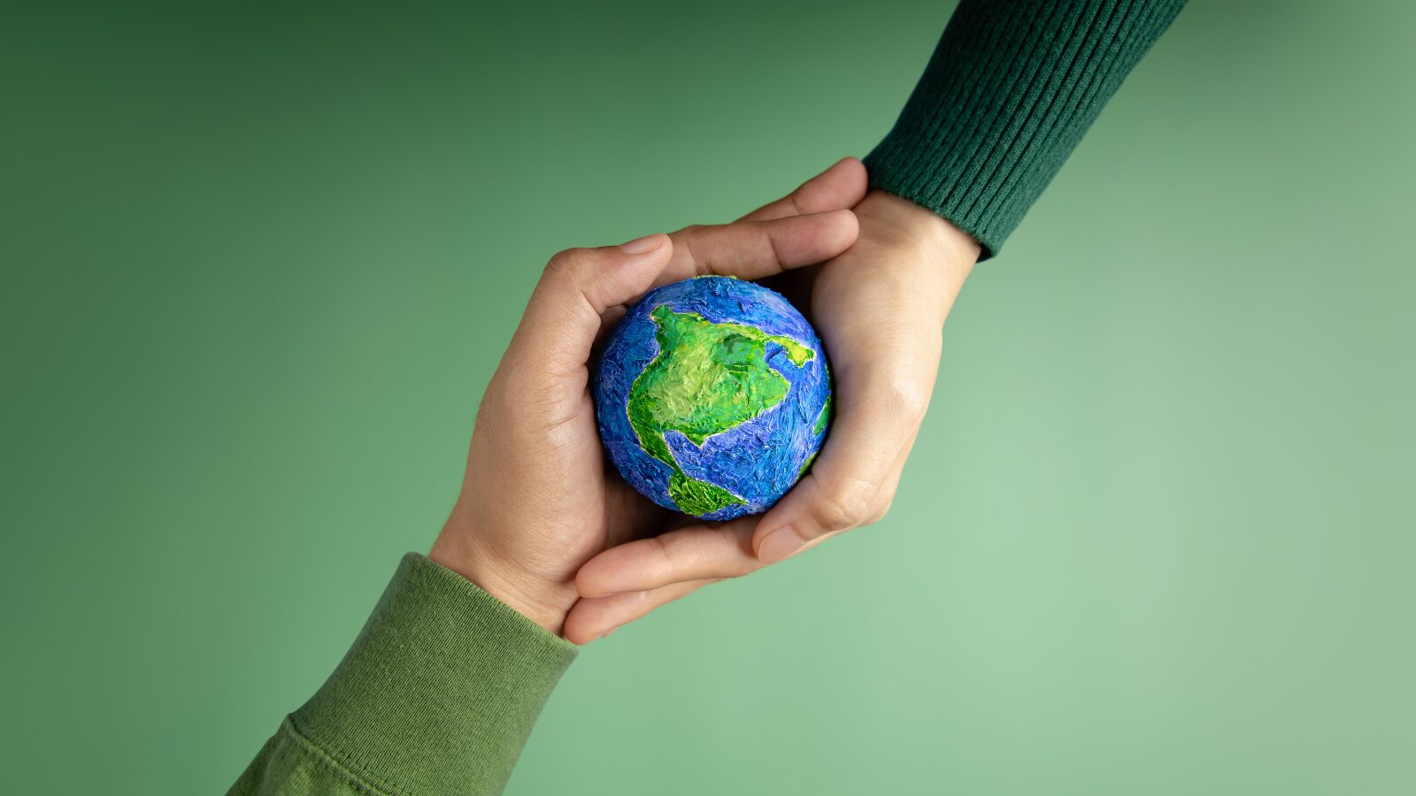 Two hands coming from opposite directions, linking together and holding 1 small globe. The images is mostly green.