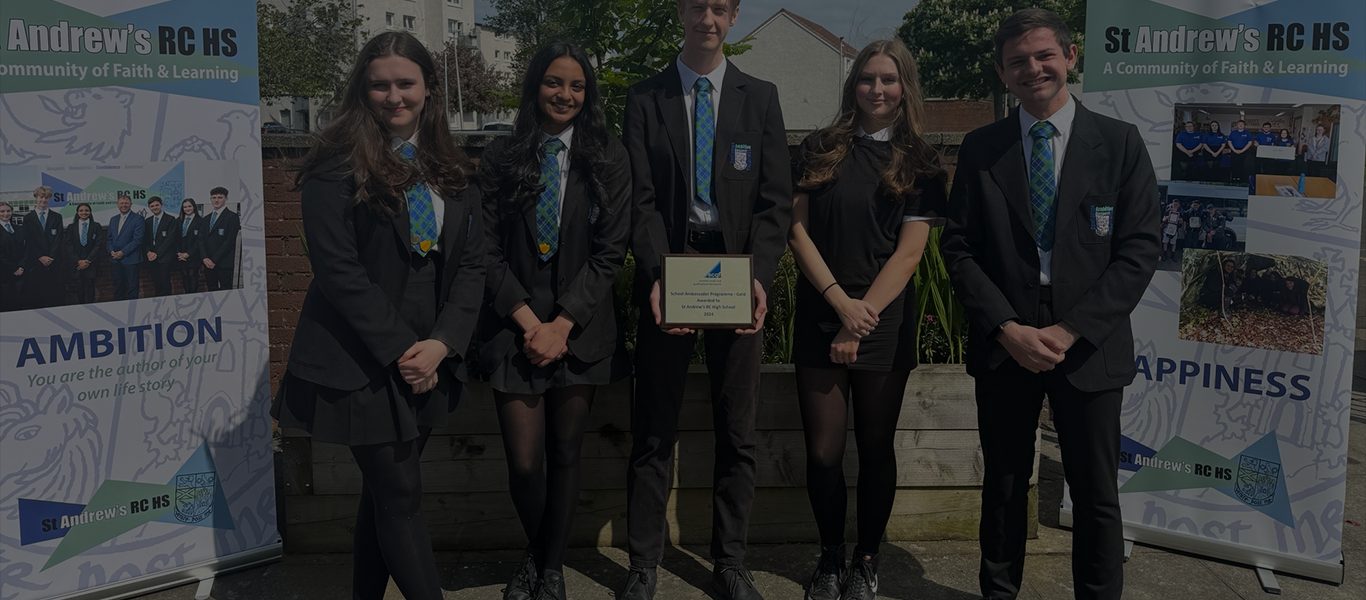A group of 5 school pupils from St Andrew's RC HS, smiling. There are banner stands promoting the school at either side of the group. They signify the support the SCQF offers to schools through the School Ambassador Programme.