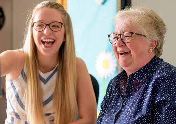 A younger and older woman sit side by side. The younger girl is pointing at something ahead. They're both laughing. They represent the age range of people that the SCQF supports.