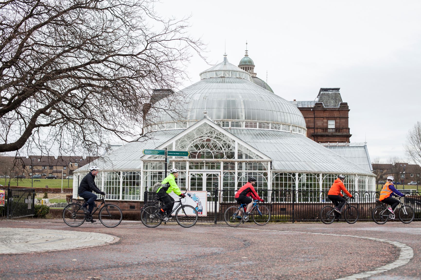 Cyclists in hi-vis vests riding bikes past People's Palace, Glasgow