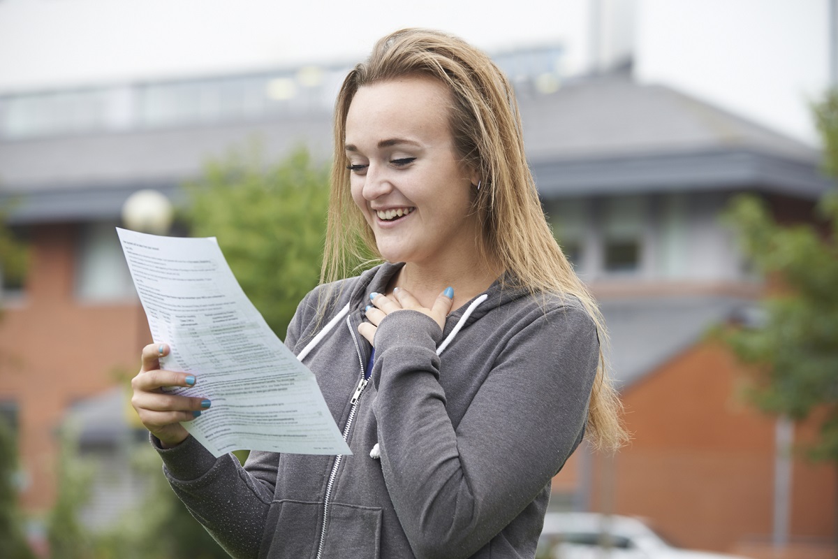 Happy teenage girl reading through her exam results letter