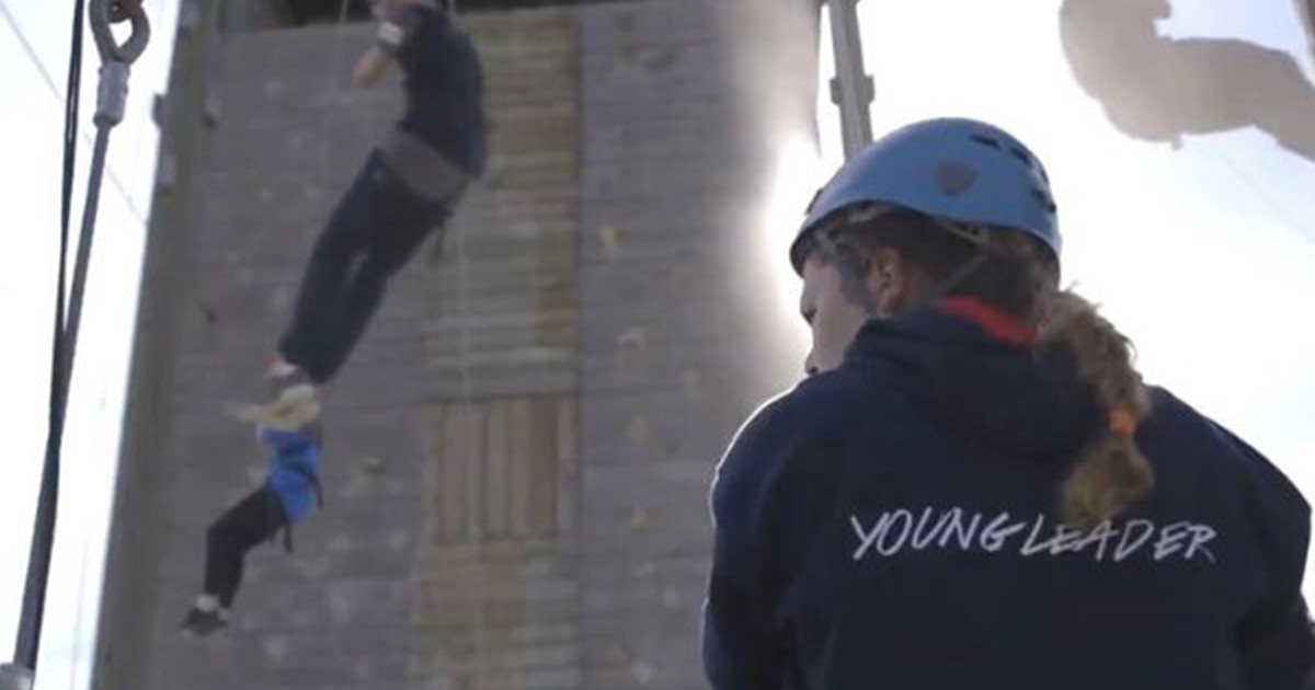 Female Young Leader student watching as fellow pupils abseil down a wall