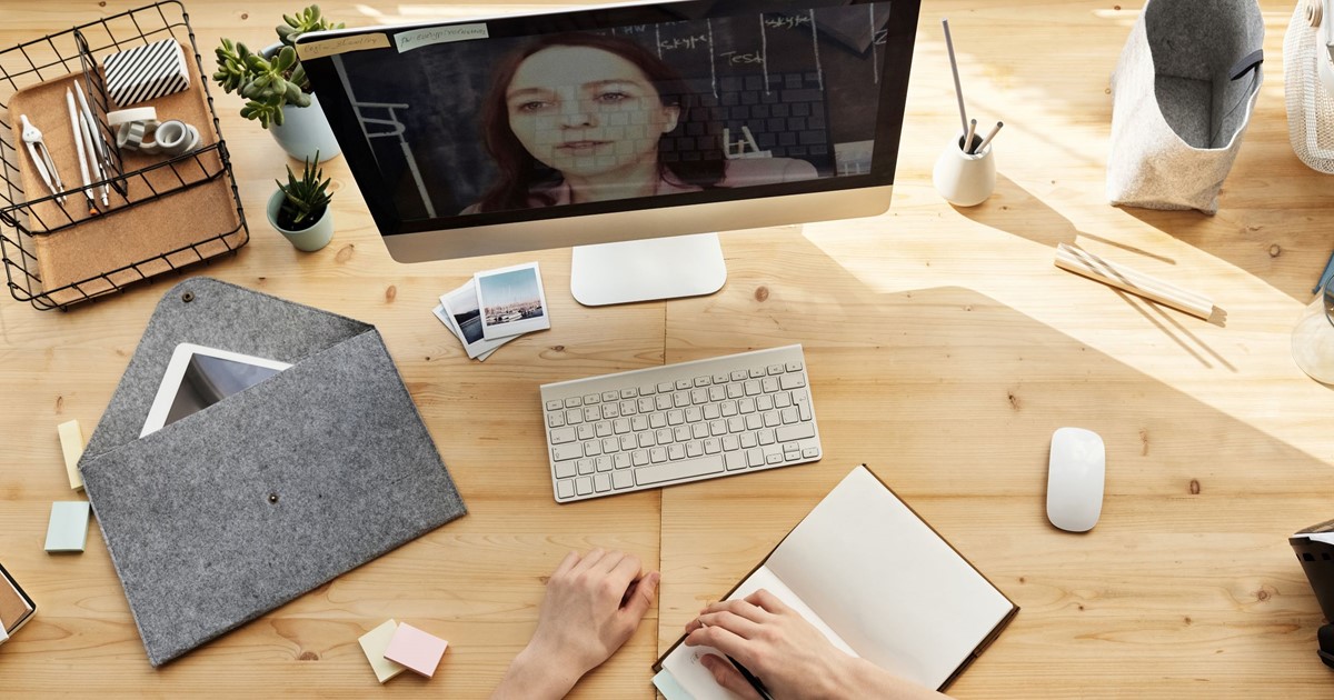 Desktop PC showing person on screen with table around it scattered with stationery items
