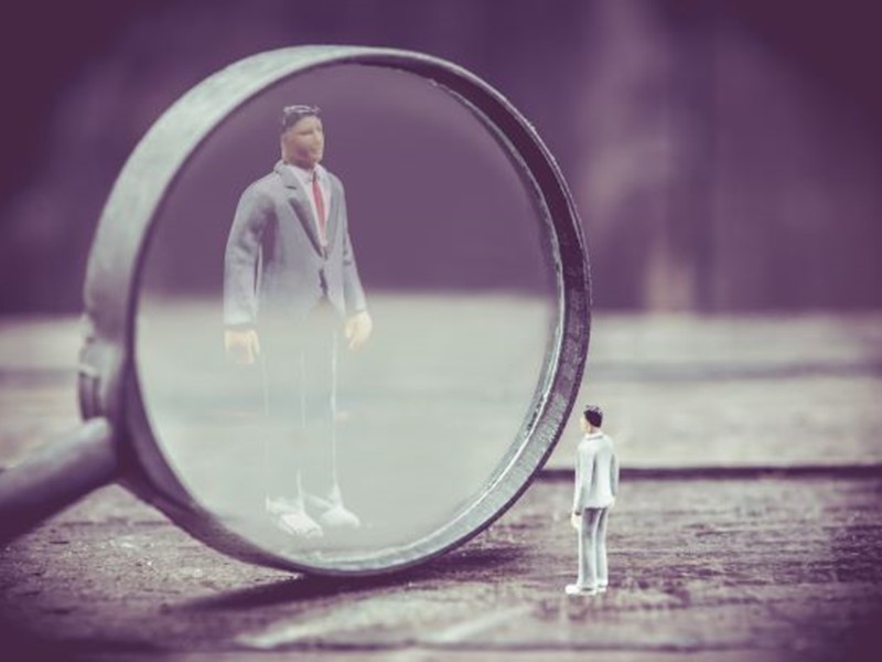 Small male figure magnified through a magnifying glass