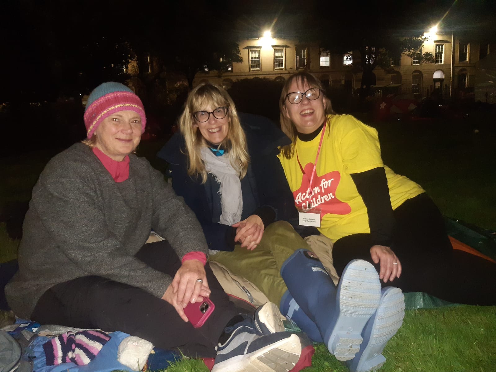 Pauline Radcliffe, Fiona Garry and Susan Lauder sit on the ground of Blythswood Square Gardens in the dark, smiling