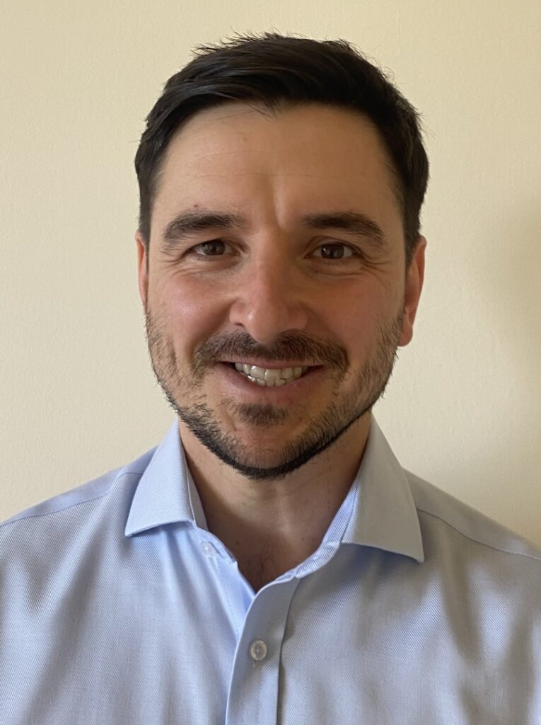 A headshot of David Balfour, who is wearing a light blue shirt and is smiling