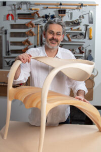 Marc Fish standing at chair that has been designed and made at his studio