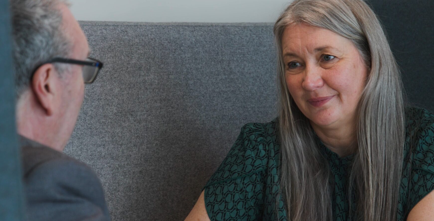 Joanne Redmond sits in a booth, smiling and listening attentively to lecturer Peter McGuire seated opposite her, suggesting a friendly conversation or interview setting.